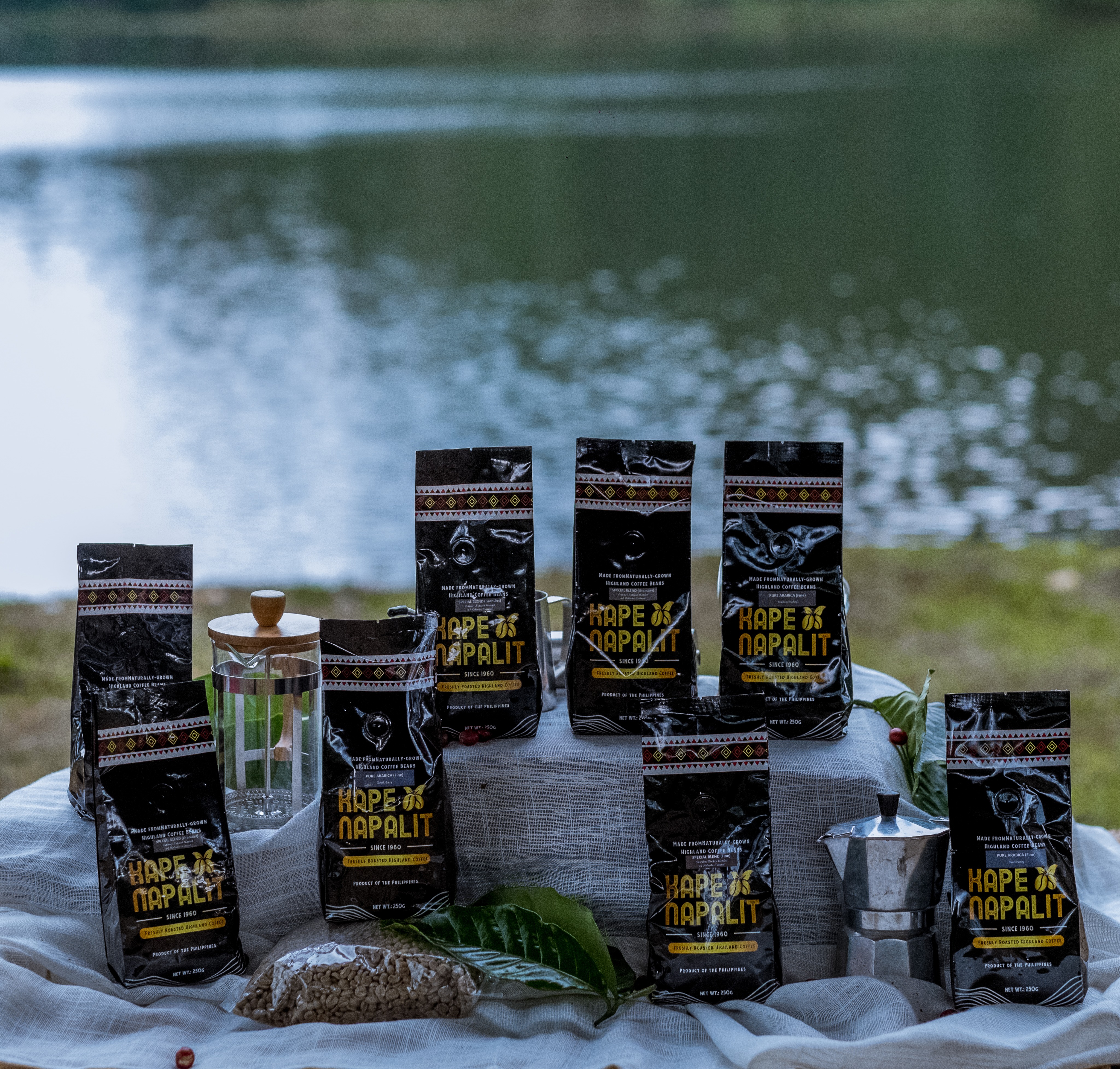 A selection of Kape Napalit coffee packages displayed with coffee leaves and brewing equipment